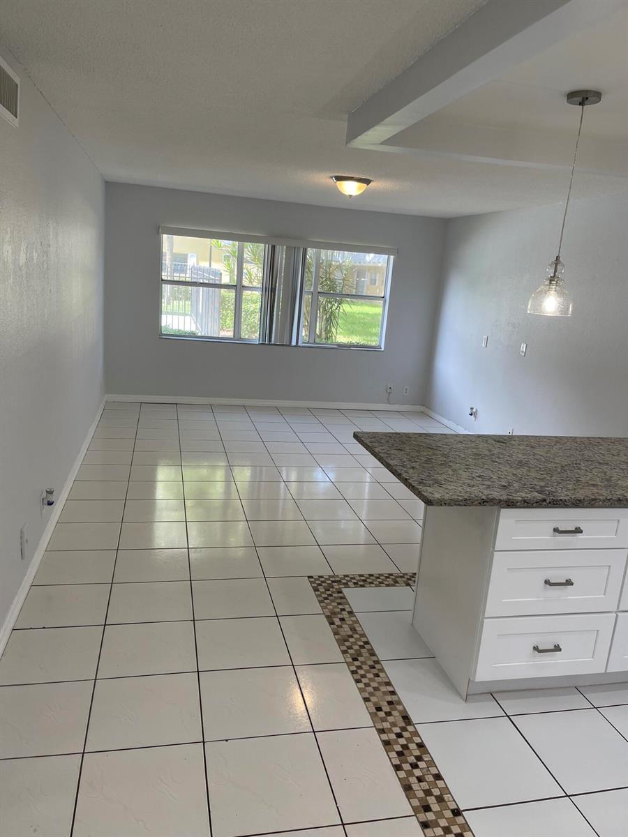 An open-concept living area features white tile flooring, a kitchen island, and a large window — 440 SE 2nd Avenue # 5, Deerfield Beach FL 33441, DEERFIELD BEACH, FL