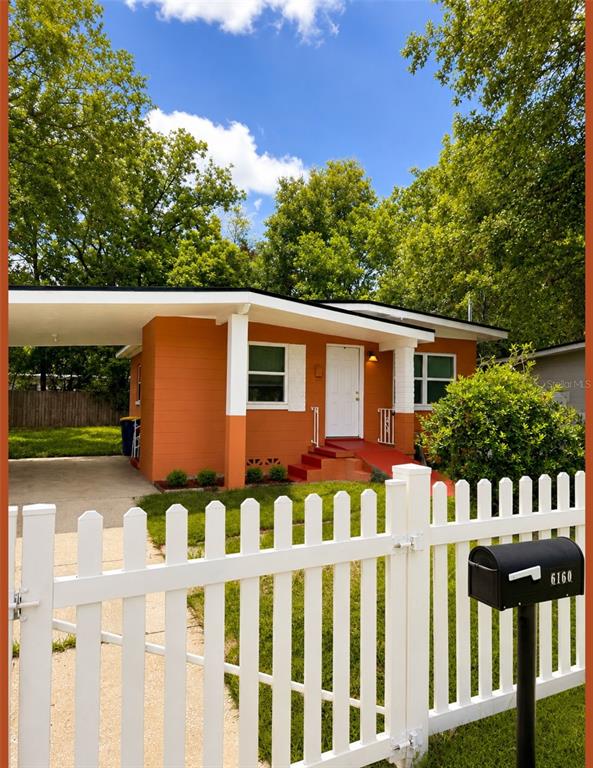 A bright orange single-story house features a white picket fence and a covered carport — 6160 STRAWFLOWER PLACE, JACKSONVILLE, FL