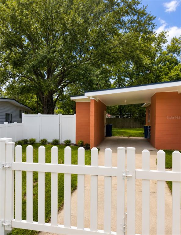 A white picket fence encloses a yard with a concrete driveway leading to a carport — 6160 STRAWFLOWER PLACE, JACKSONVILLE, FL