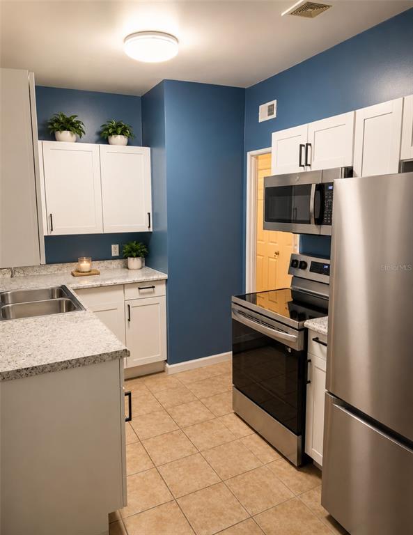 A kitchen features white cabinets, granite countertops, stainless steel appliances, and blue walls — 6160 STRAWFLOWER PLACE, JACKSONVILLE, FL