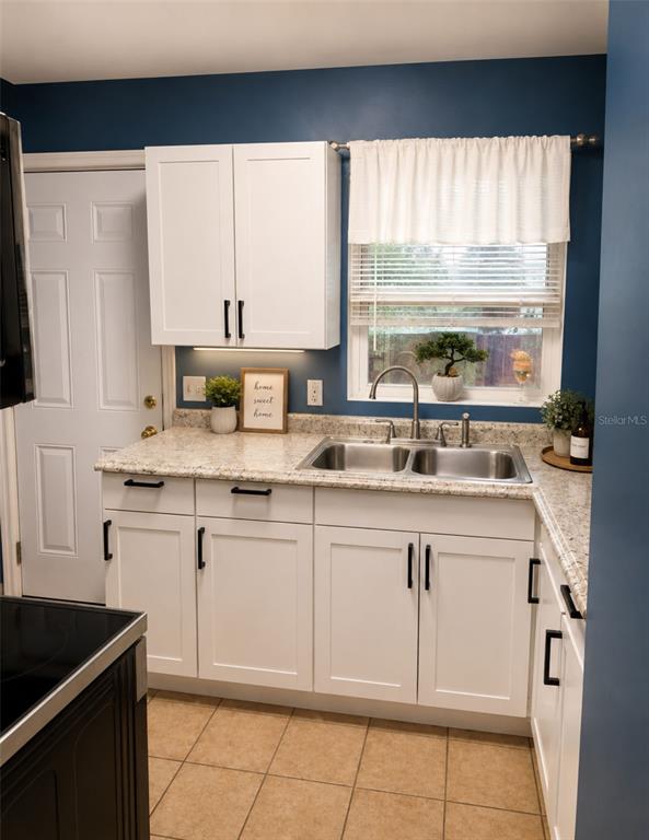 A kitchen features white cabinets, granite countertops, a double-basin sink, and dark blue walls — 6160 STRAWFLOWER PLACE, JACKSONVILLE, FL