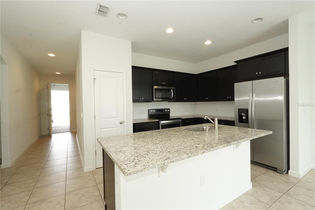 A kitchen features dark cabinets, granite countertops, a center island, and stainless steel appliances — 3552 PATRON AVENUE, DELTONA, FL