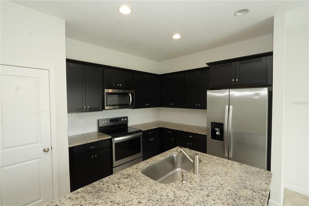 A kitchen features dark cabinets, granite countertops, stainless steel appliances, and a central island sink — 3552 PATRON AVENUE, DELTONA, FL