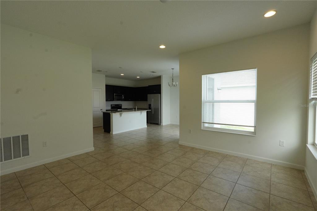 An open-concept living area with tile flooring leads to a kitchen with dark cabinetry — 3552 PATRON AVENUE, DELTONA, FL