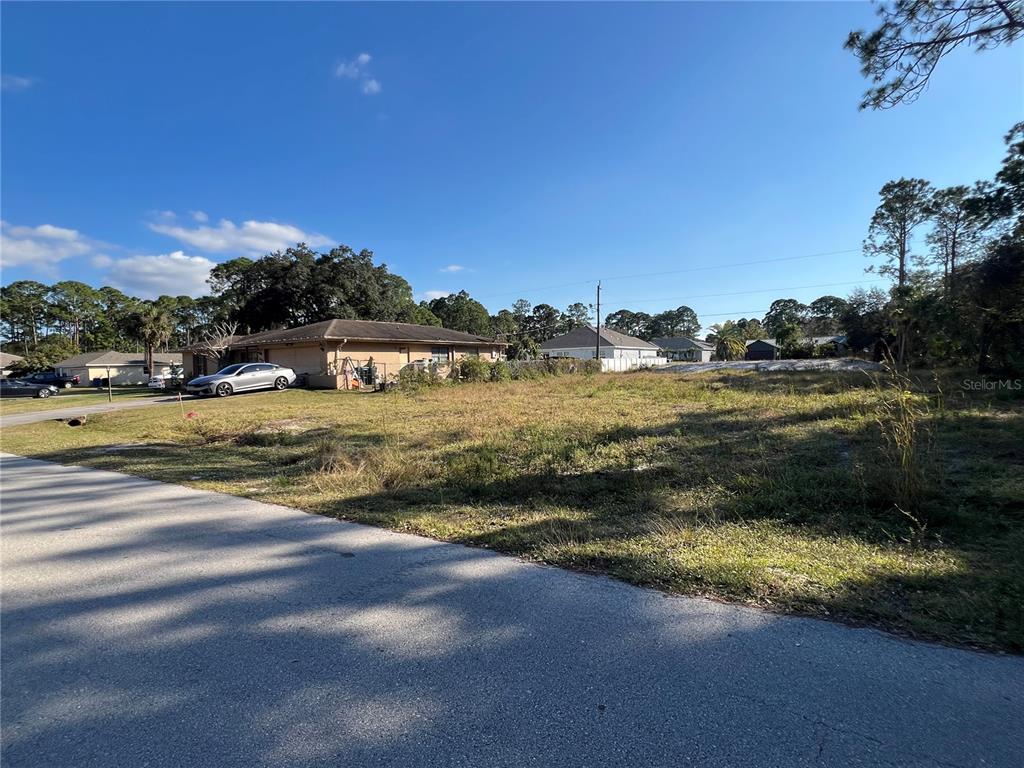 A vacant, grassy residential lot sits beside a house and a paved street — 442 LACKLAND STREET SW, PALM BAY, FL