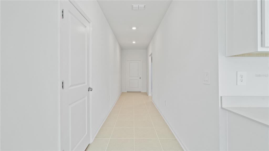 A bright, narrow hallway with white walls, tile flooring, and a closed door at the end — 1947 PINE MEADOWS GOLFCOURSE ROAD, EUSTIS, FL