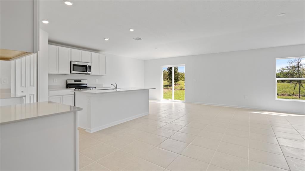 A bright kitchen with white cabinets and an island opens to a tiled living area — 1947 PINE MEADOWS GOLFCOURSE ROAD, EUSTIS, FL