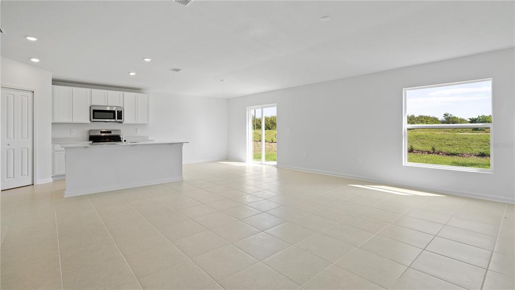An open-concept kitchen and living area features white cabinetry, tile flooring, and a sliding door — 1947 PINE MEADOWS GOLFCOURSE ROAD, EUSTIS, FL