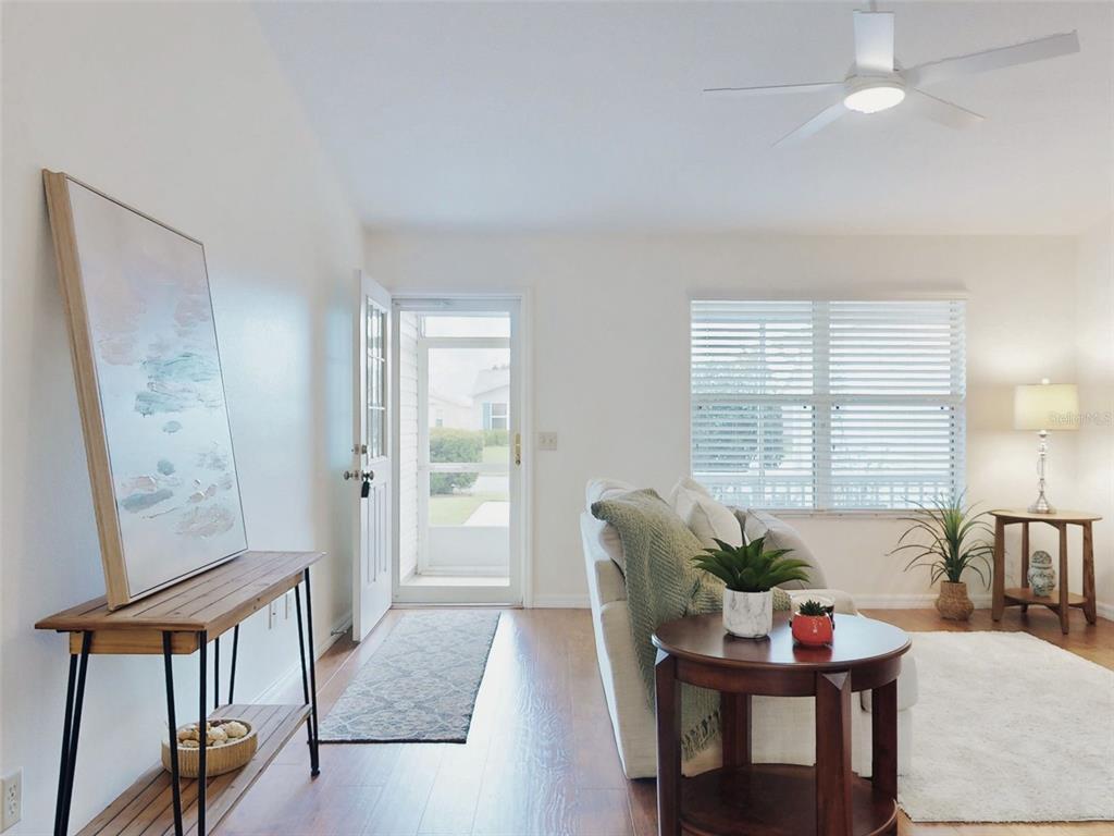 A living room features a front door, wood flooring, a ceiling fan, and a console table — 1521 HOLLYBERRY PLACE, THE VILLAGES, FL