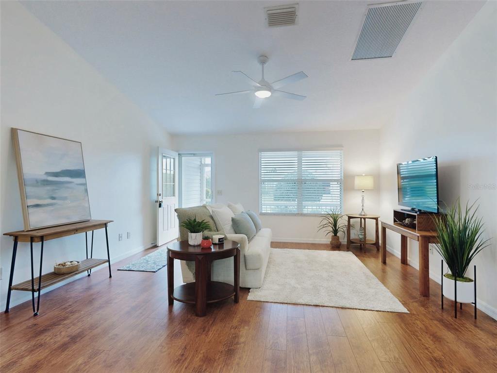 A living room features wood-look flooring, a white sofa, a ceiling fan, and a television — 1521 HOLLYBERRY PLACE, THE VILLAGES, FL