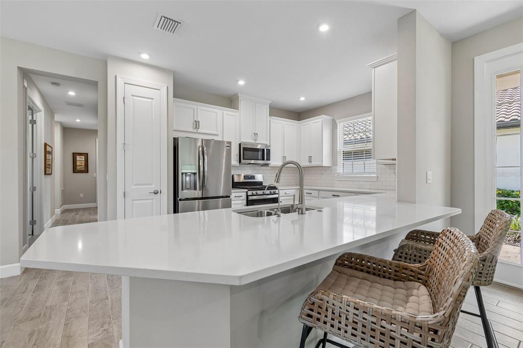 A kitchen with white cabinets, a quartz island, stainless steel appliances, and two wicker chairs — 4333 CAIROLI COURT, WESLEY CHAPEL, FL