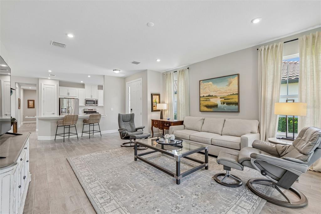 A bright living room features a sofa, two recliners, a glass coffee table, and an open kitchen — 4333 CAIROLI COURT, WESLEY CHAPEL, FL