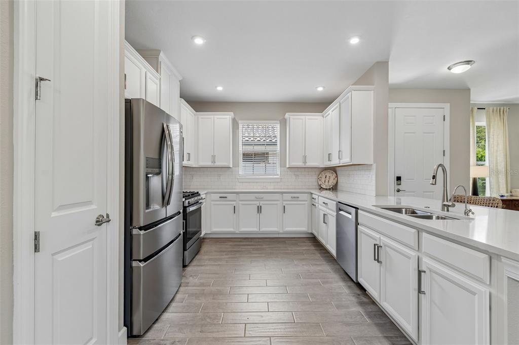 A kitchen with white cabinets, stainless steel appliances, quartz countertops, and wood-look tile flooring — 4333 CAIROLI COURT, WESLEY CHAPEL, FL