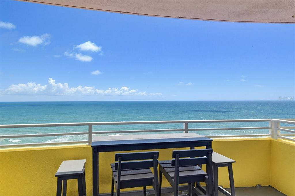 A balcony with a table and chairs overlooks the ocean under a blue sky — 300 N ATLANTIC AVENUE UNIT 1505, DAYTONA BEACH, FL