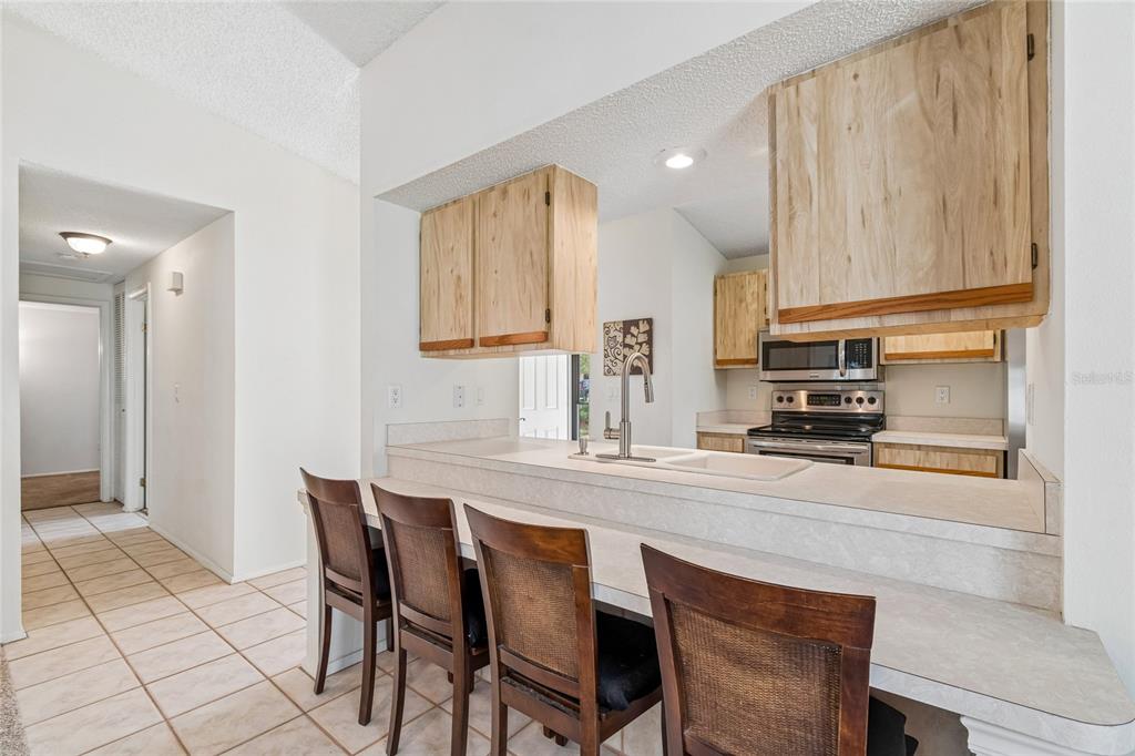 A kitchen with light wood cabinets, a breakfast bar, and four dark wooden chairs — 10305 TURKEY OAK DRIVE, NEW PORT RICHEY, FL