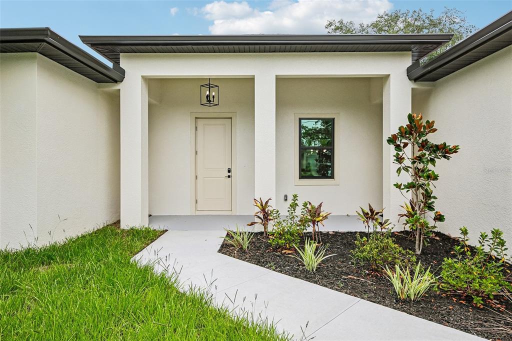 A white house exterior features a covered entryway with a door, window, and landscaping — 2792 ABBEVILLE ROAD, NORTH PORT, FL