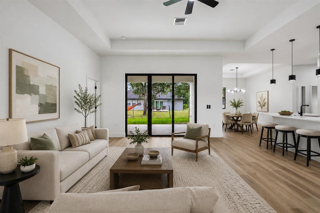 A bright, open-concept living room features light wood floors, a neutral sofa, and sliding glass doors — 2792 ABBEVILLE ROAD, NORTH PORT, FL