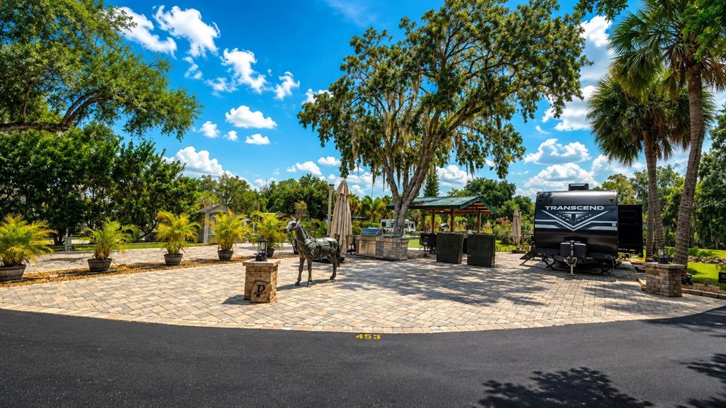 A paved outdoor patio features a horse statue, a travel trailer, and a covered kitchen area — 453 WATERWAY DRIVE, LAKE WALES, FL