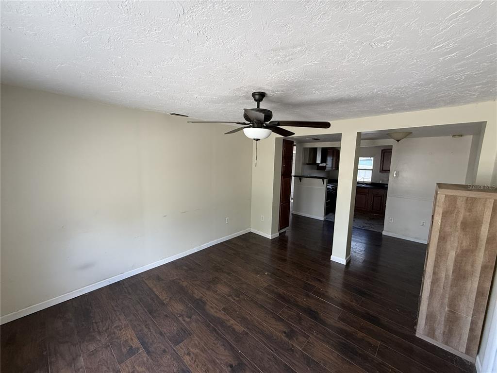 A living room with dark wood flooring, a ceiling fan, and an open kitchen view — 1810 9TH STREET W, PALMETTO, FL