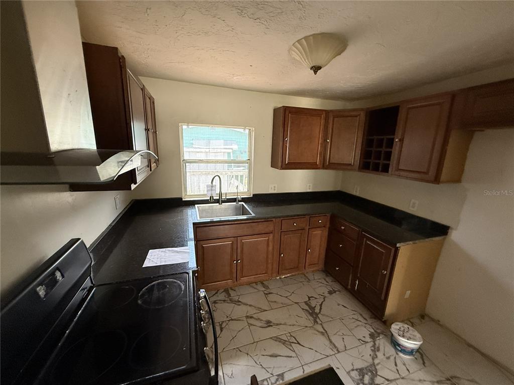 A kitchen features dark wood cabinets, black countertops, a stainless steel sink, and marble-patterned flooring — 1810 9TH STREET W, PALMETTO, FL