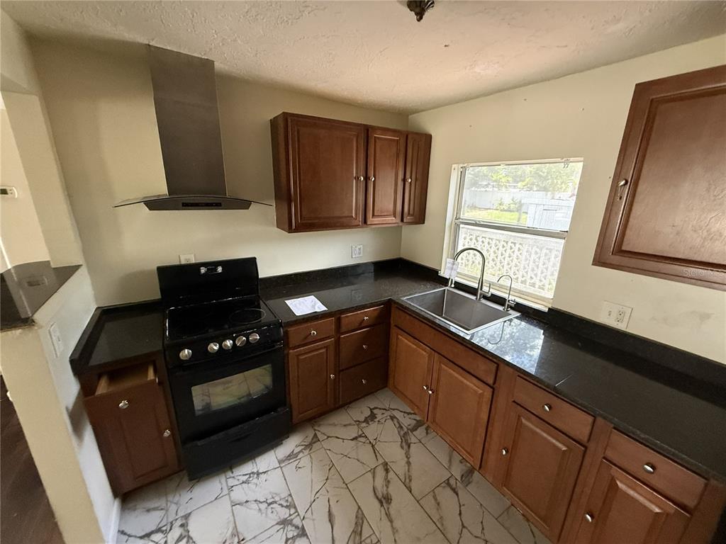 A kitchen with dark wood cabinets, black countertops, a stainless steel range hood, and tile flooring — 1810 9TH STREET W, PALMETTO, FL