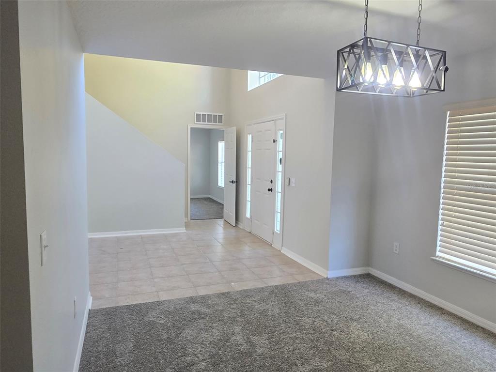 A room with gray carpet and tile flooring features a modern chandelier and front door — 3001 MANDOLIN DRIVE, KISSIMMEE, FL