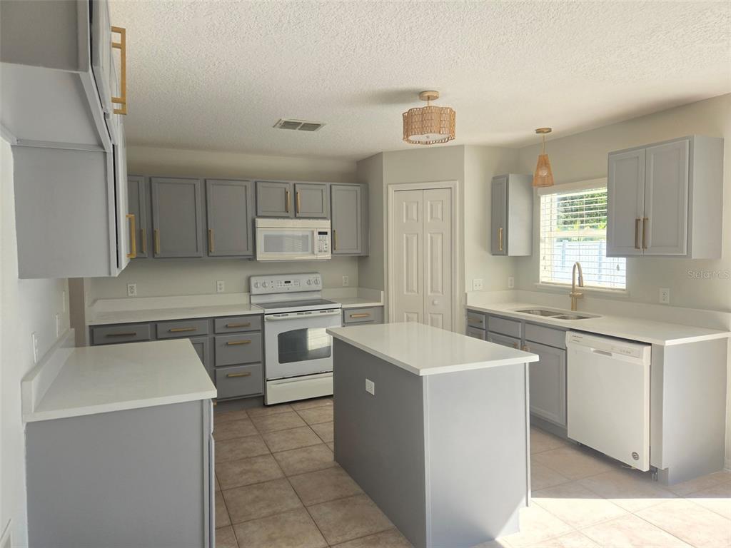 A kitchen features gray cabinets, white countertops, a center island, and stainless steel appliances — 3001 MANDOLIN DRIVE, KISSIMMEE, FL