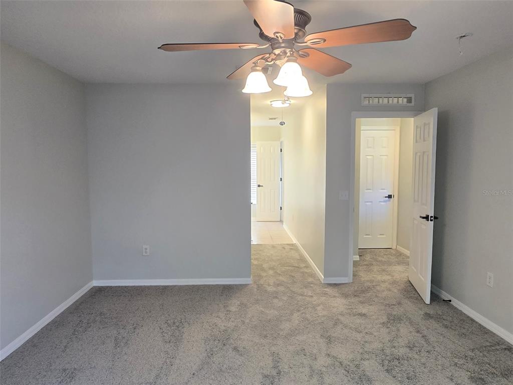 A carpeted room features a ceiling fan, a doorway to a hallway, and an open door — 3001 MANDOLIN DRIVE, KISSIMMEE, FL