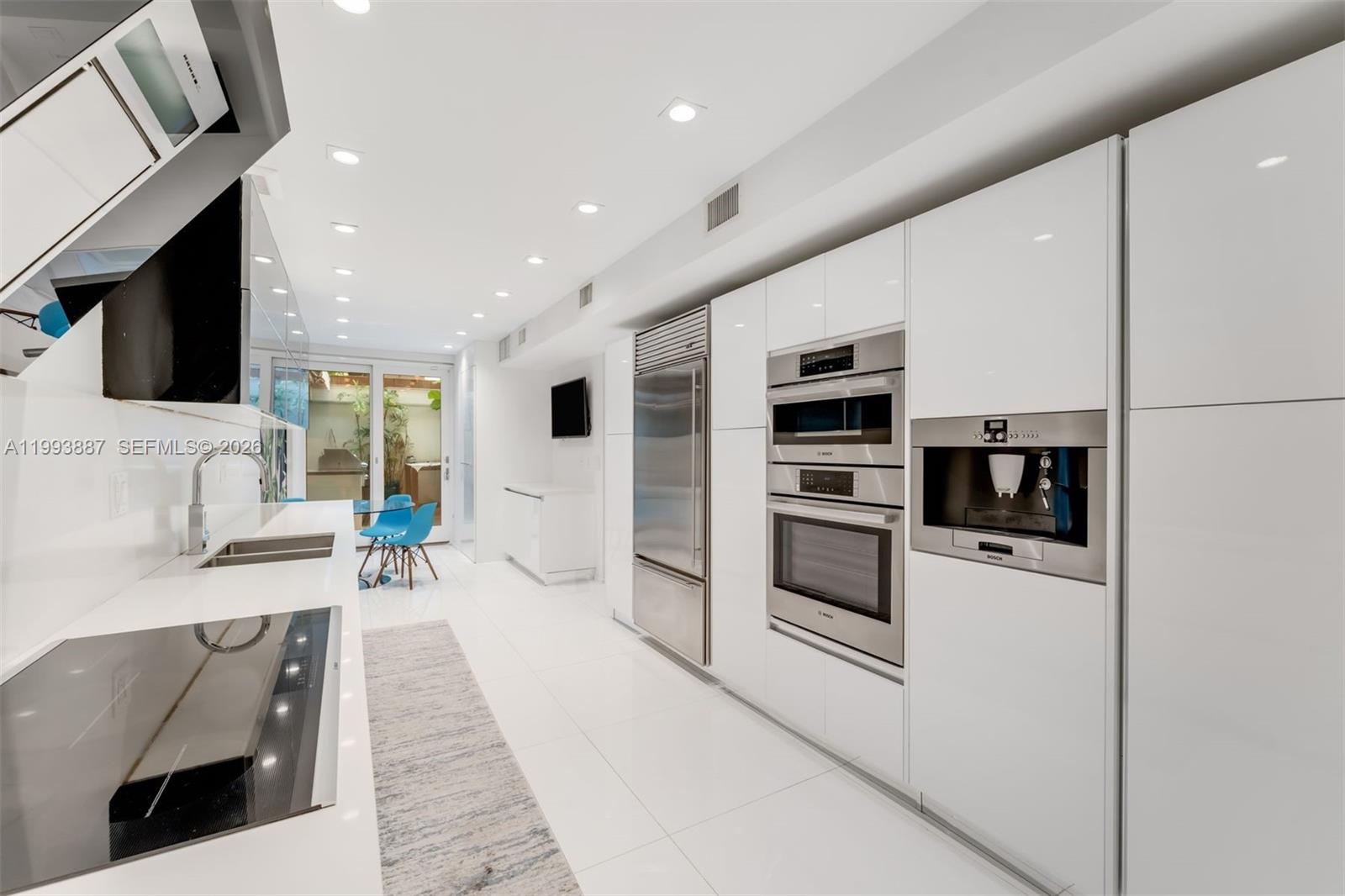 A modern white kitchen features stainless steel appliances, glossy cabinetry, and a tile floor — 1524 NE Quayside Ter # A4, Miami FL 33138, MIAMI, FL