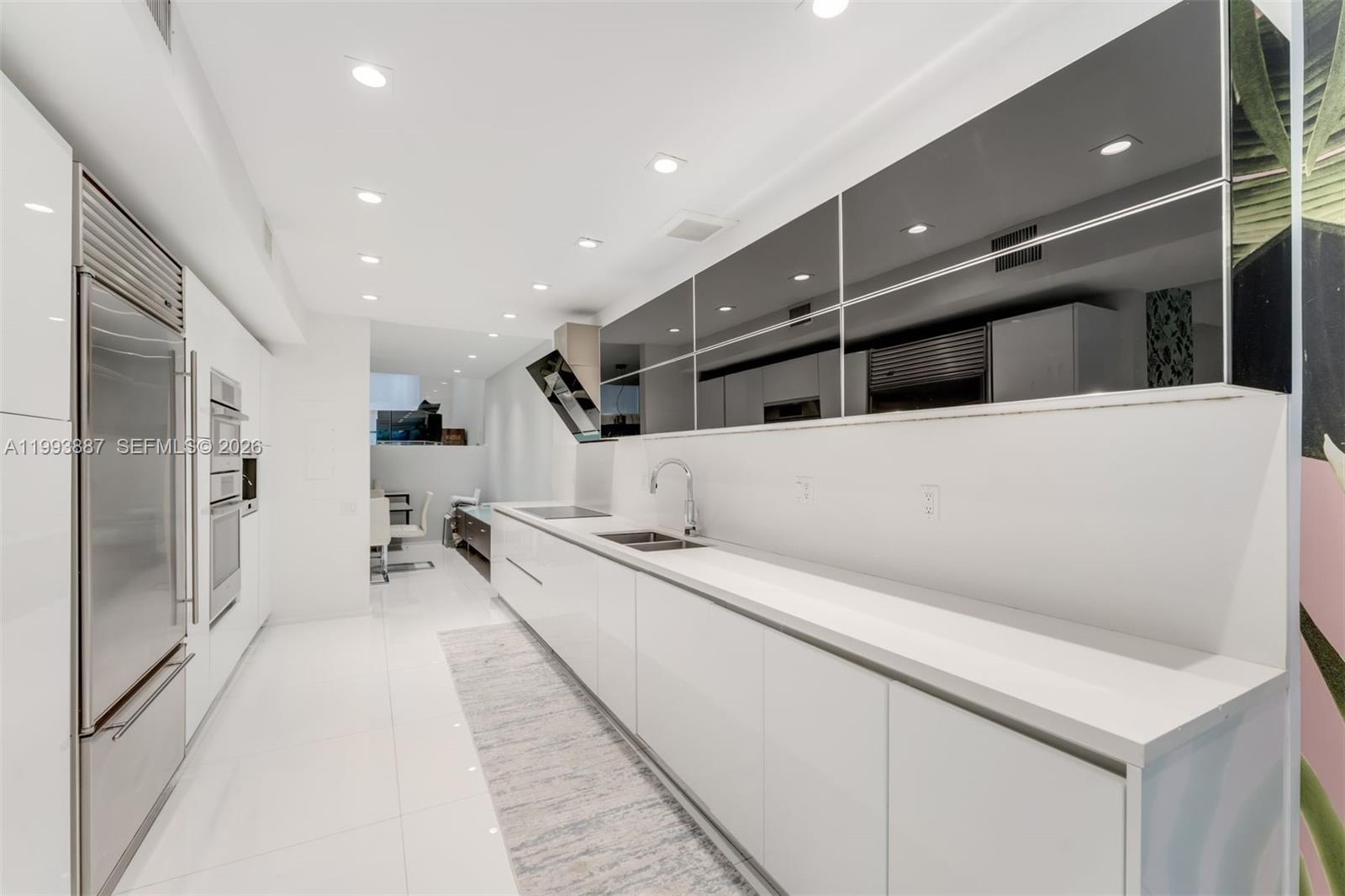 A modern white kitchen features sleek cabinetry, stainless steel appliances, and a long countertop — 1524 NE Quayside Ter # A4, Miami FL 33138, MIAMI, FL