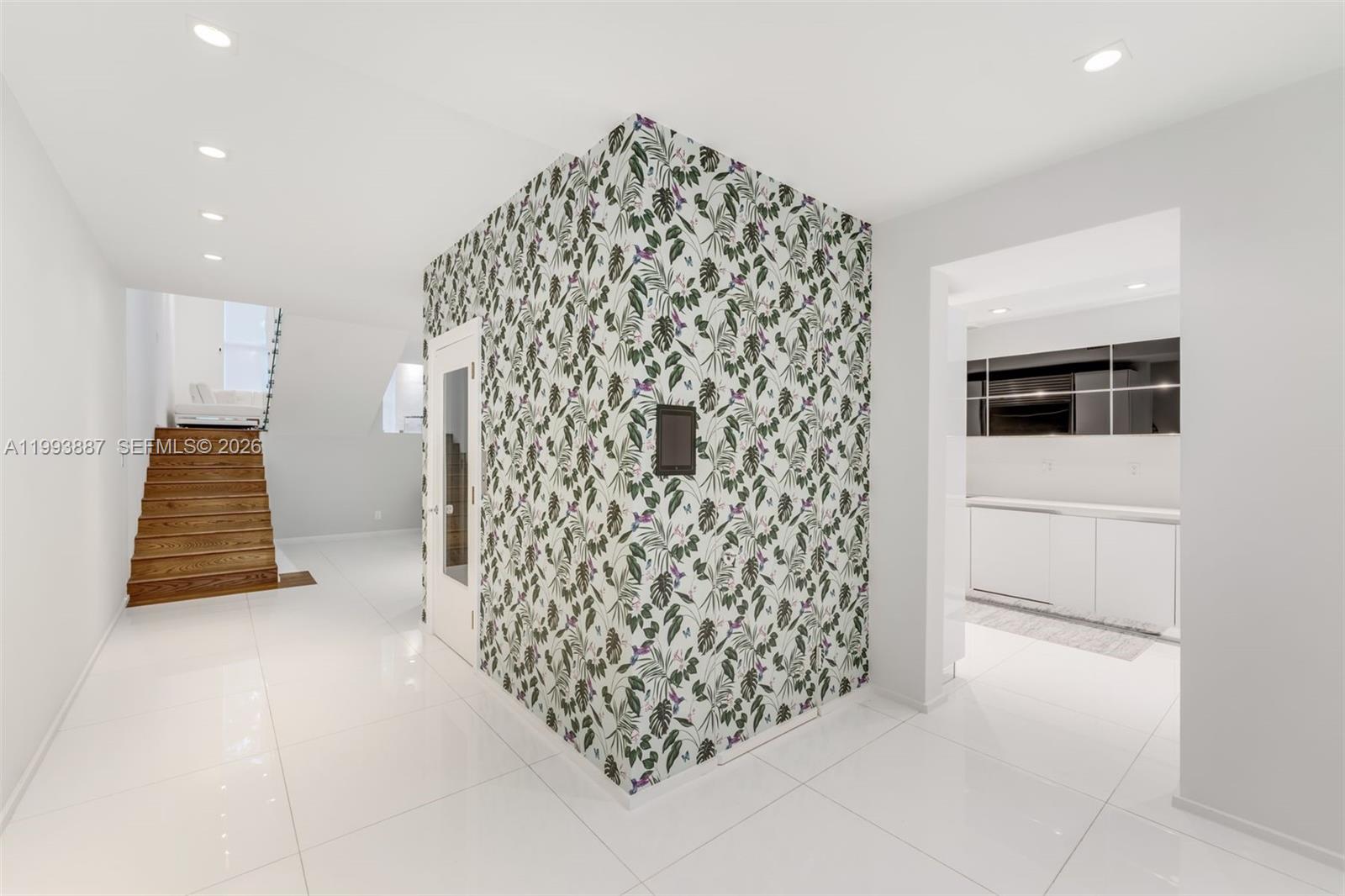 A white-tiled room features a central wall covered in tropical-patterned wallpaper and wooden stairs — 1524 NE Quayside Ter # A4, Miami FL 33138, MIAMI, FL