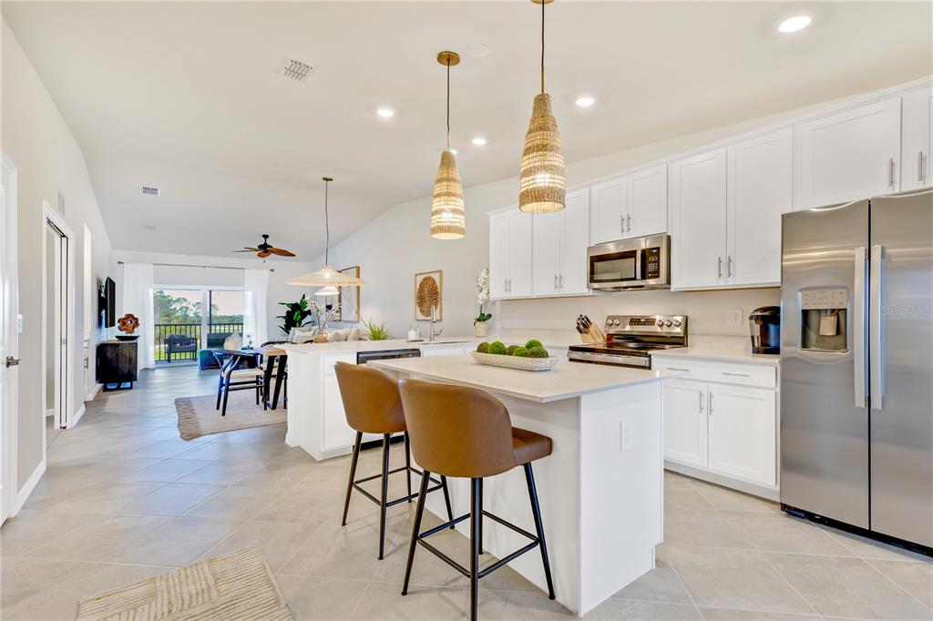 A modern kitchen with white cabinets, a central island with bar stools, and stainless appliances — 17440 OPAL SAND DRIVE UNIT 202, VENICE, FL