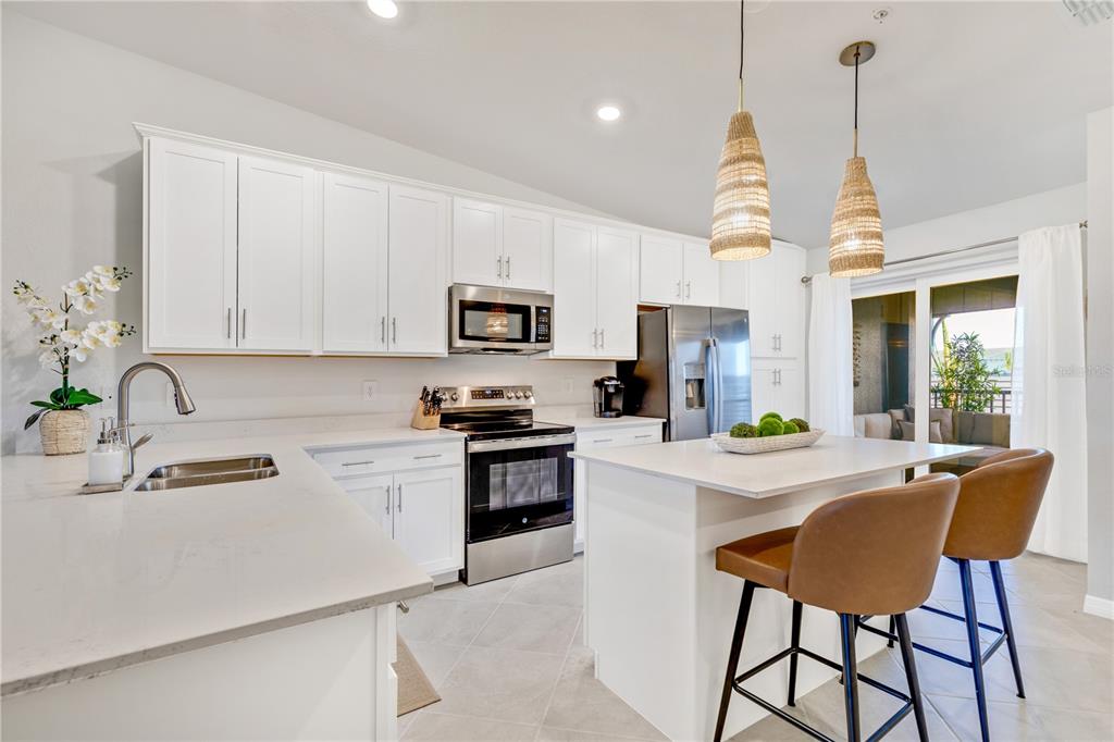 A modern kitchen features white cabinets, stainless steel appliances, a center island, and two barstools — 17440 OPAL SAND DRIVE UNIT 202, VENICE, FL