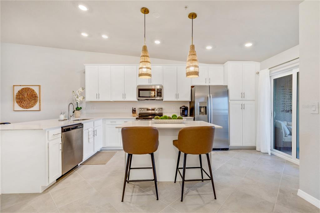 A modern kitchen features white cabinetry, stainless steel appliances, a center island, and two barstools — 17440 OPAL SAND DRIVE UNIT 202, VENICE, FL