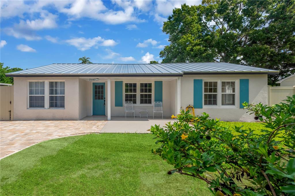 A single-story house with a metal roof, light-colored stucco, and blue shutters and door — 2541 47TH AVENUE N, ST PETERSBURG, FL