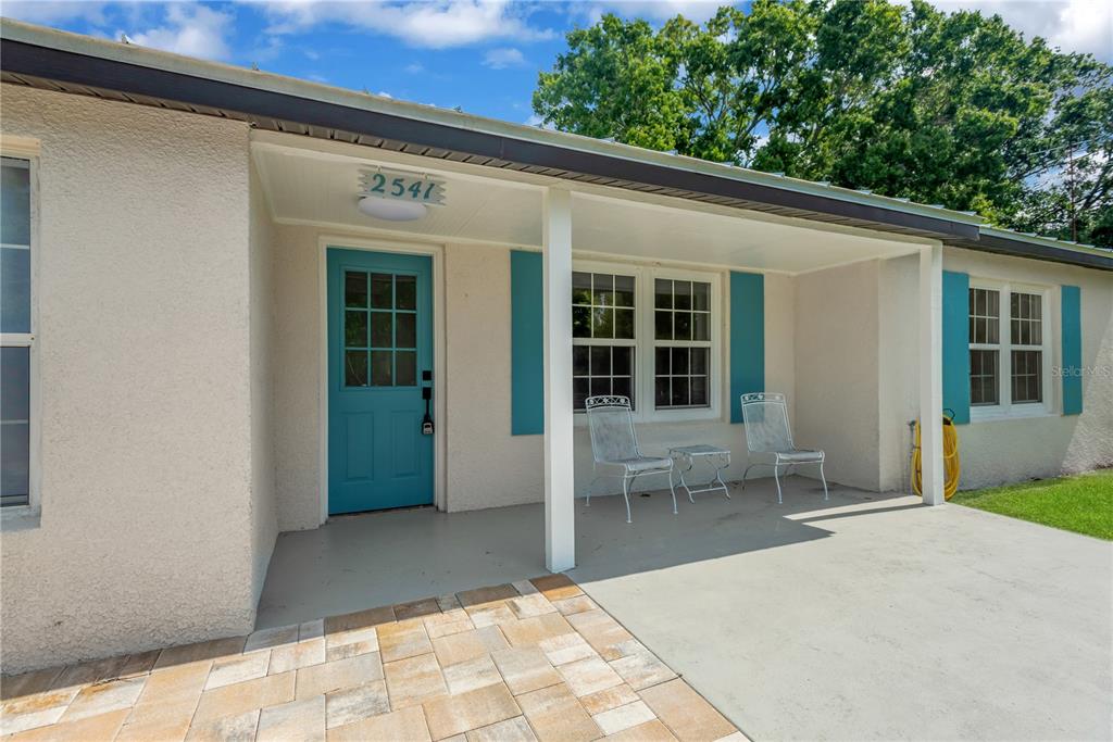 A covered front porch features a teal door, white shutters, and two metal chairs — 2541 47TH AVENUE N, ST PETERSBURG, FL