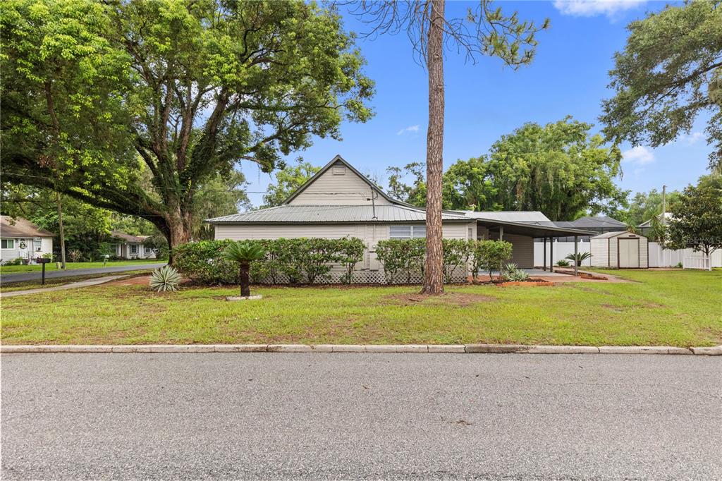 A single-story house with a metal roof, a carport, and a large tree in front — 5450 10TH STREET, ZEPHYRHILLS, FL