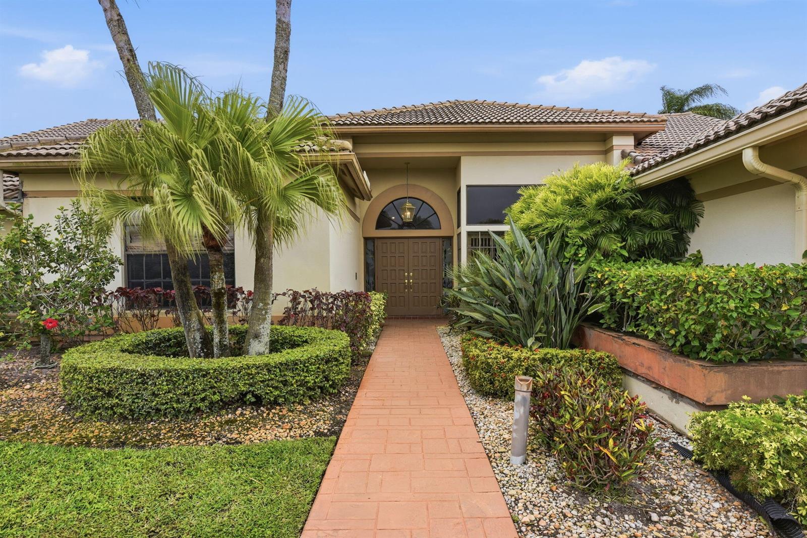 A paved walkway leads to the front entrance of a house with tropical landscaping — 10330 Silver Lake Drive, Boca Raton FL 33428, BOCA RATON, FL
