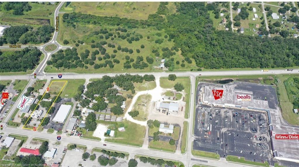 This aerial view shows a vacant lot outlined in yellow near a commercial shopping center — 939 S 6TH AVENUE, WAUCHULA, FL