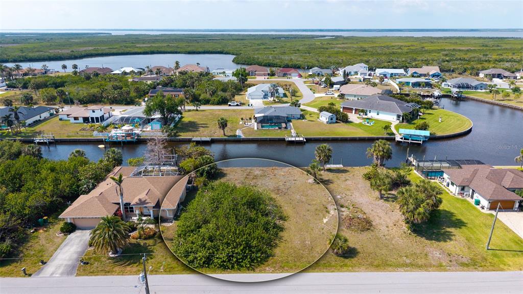 An aerial view shows a vacant waterfront lot highlighted by a circle next to a house — 17117 CANARY LANE, PORT CHARLOTTE, FL