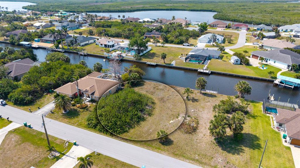 An aerial view shows a vacant waterfront lot with a circular highlight next to a house — 17117 CANARY LANE, PORT CHARLOTTE, FL