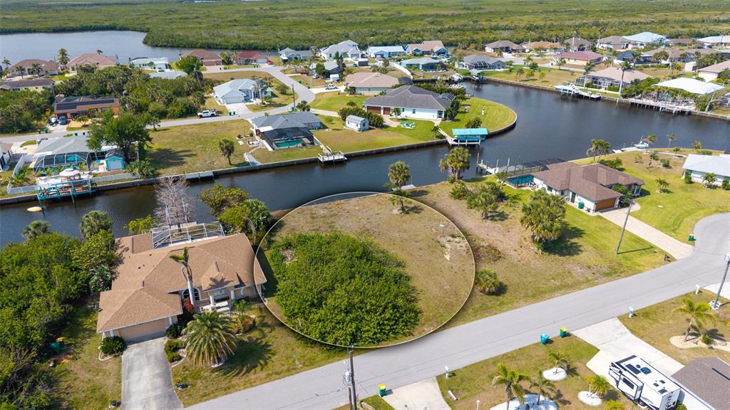 An aerial view shows a vacant, circular-highlighted residential lot situated along a canal — 17117 CANARY LANE, PORT CHARLOTTE, FL