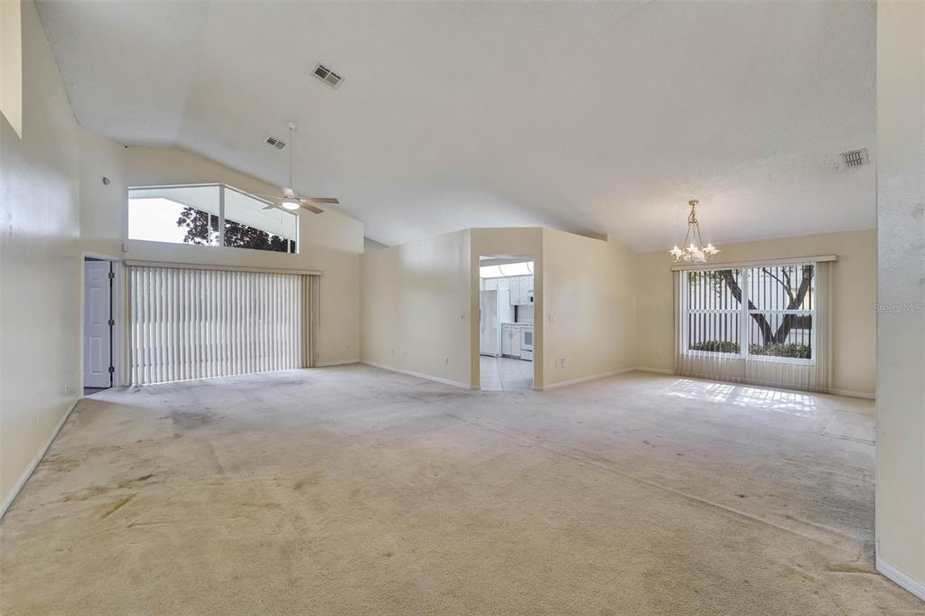 A spacious living area features vaulted ceilings, beige wall-to-wall carpeting, and large windows with blinds — 6541 COUNTRY RIDGE LANE, NEW PORT RICHEY, FL