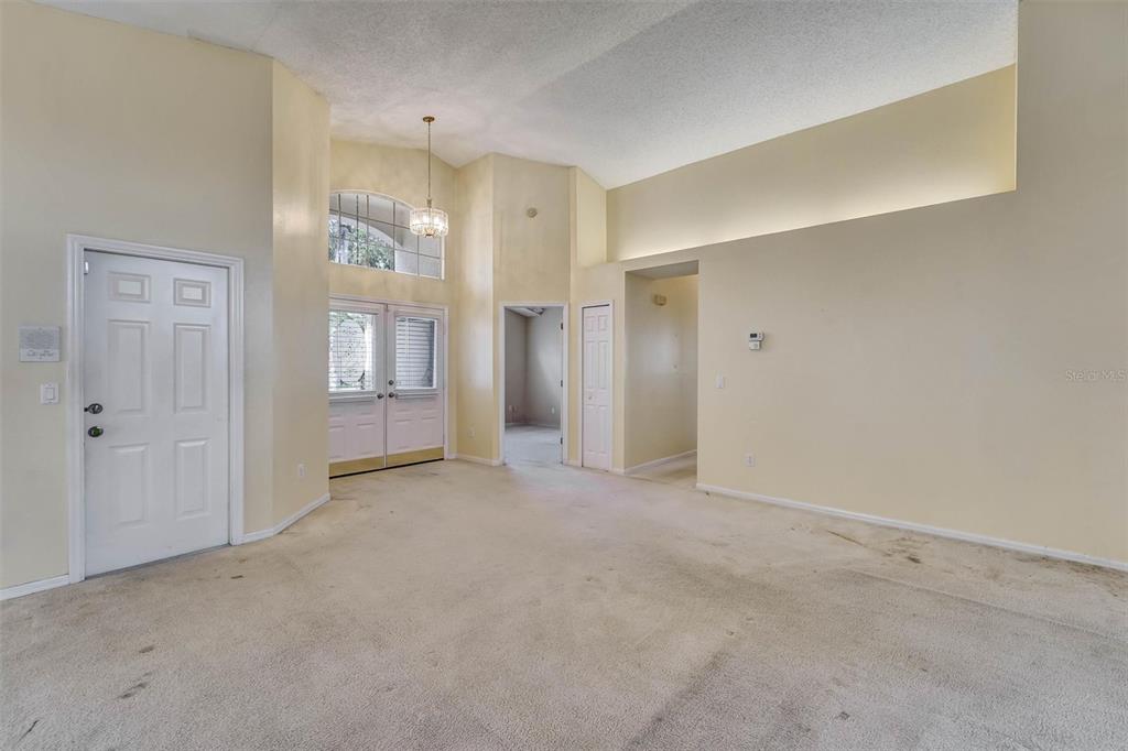 An empty living room features high ceilings, beige carpeting, and a white double-door entryway — 6541 COUNTRY RIDGE LANE, NEW PORT RICHEY, FL