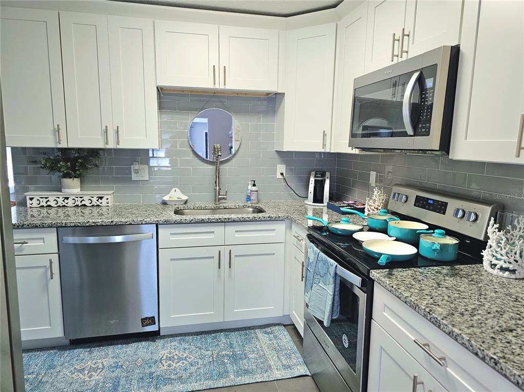 A kitchen features white cabinets, granite countertops, a gray subway tile backsplash, and stainless appliances — 2035 28TH AVENUE N, ST PETERSBURG, FL