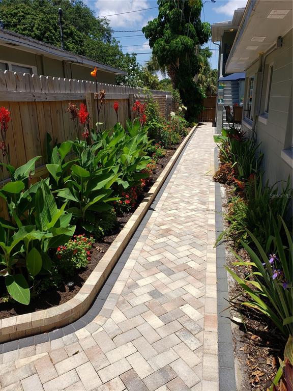 A paved walkway runs between a wooden fence with garden beds and the side of a house — 2035 28TH AVENUE N, ST PETERSBURG, FL
