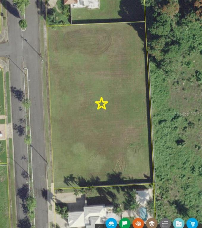 This aerial view shows a rectangular, vacant grass lot bordered by a road and trees — Hacienda El Molino A-10 CALLE PASEO MADRID, VEGA ALTA, PR