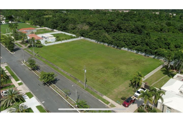An aerial view shows a large, vacant grassy lot situated between residential houses and trees — Hacienda El Molino A-10 CALLE PASEO MADRID, VEGA ALTA, PR
