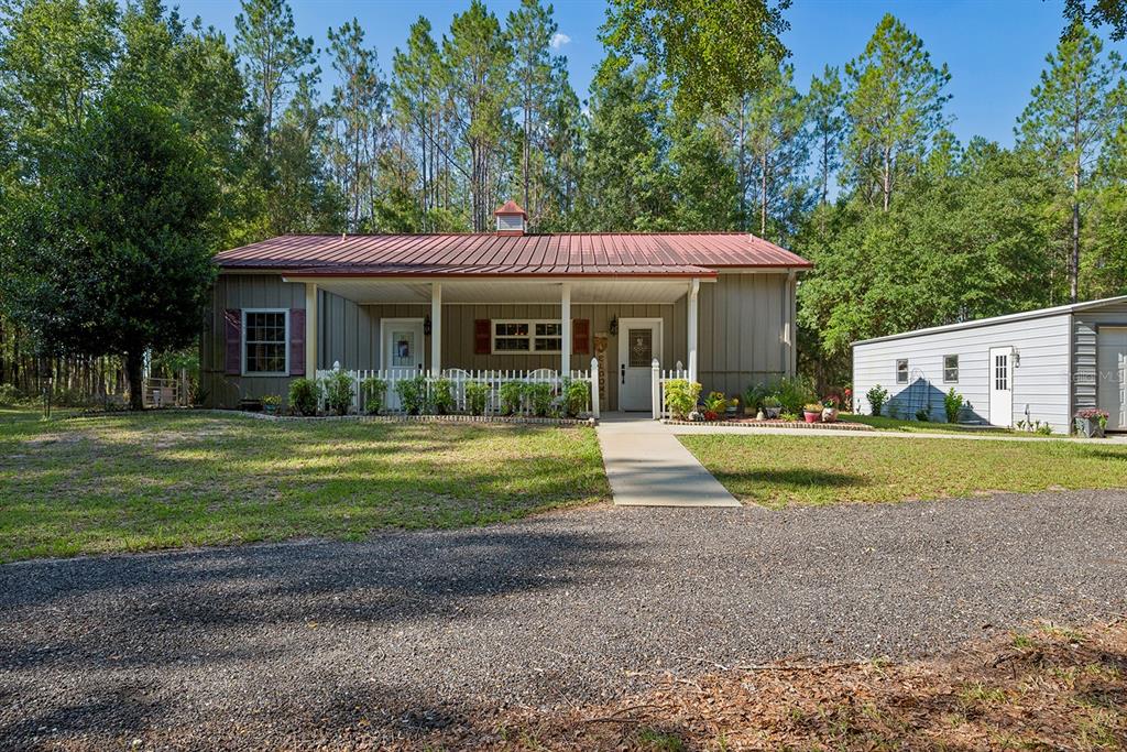 A single-story house with a metal roof and front porch sits near a metal garage — 14590 NE 35TH AVENUE, CHIEFLAND, FL