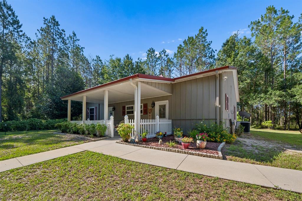 A single-story house with a covered front porch and white picket fence in a wooded area — 14590 NE 35TH AVENUE, CHIEFLAND, FL